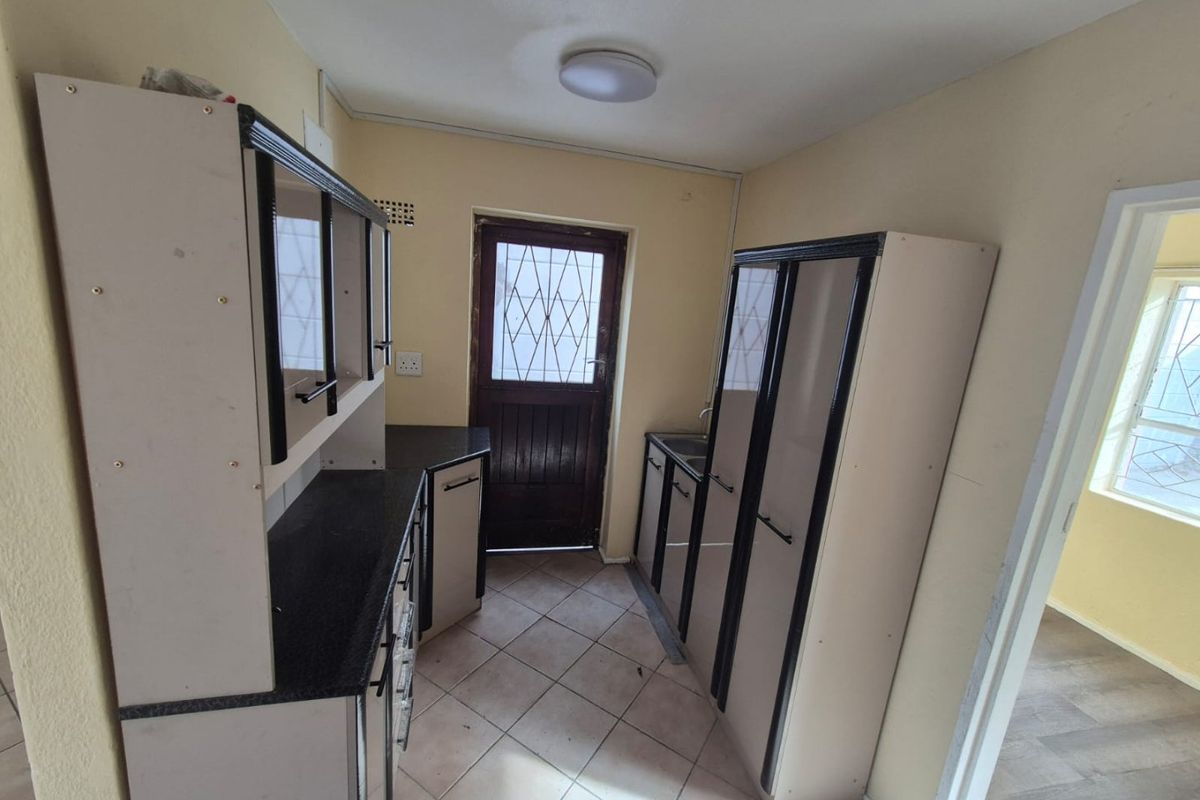 A compact kitchen featuring built-in cabinetry, laminate countertops, and tiled flooring, with direct access to an exterior door.
