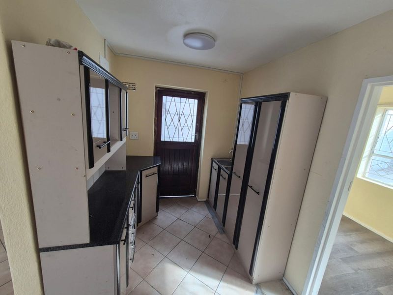A compact kitchen featuring built-in cabinetry, laminate countertops, and tiled flooring, with direct access to an exterior door.