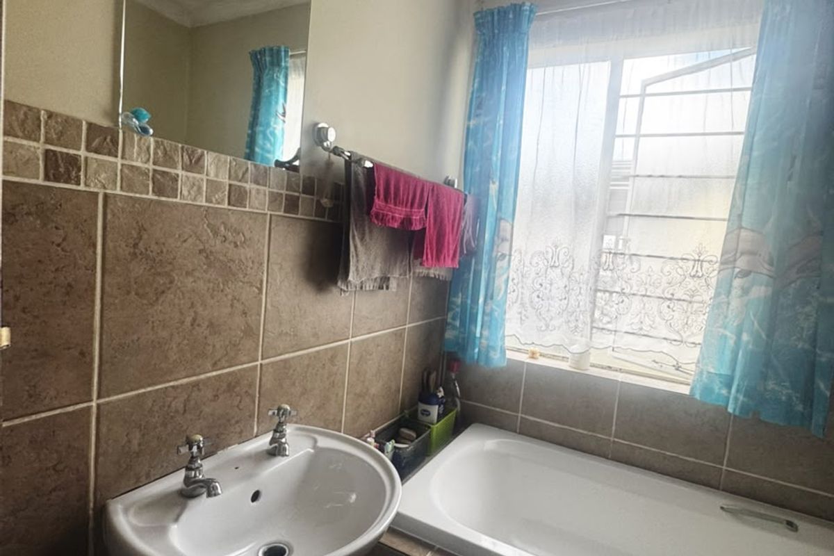 A functional bathroom featuring a pedestal basin, built-in bathtub, and tiled wall finishes with a window providing natural light.