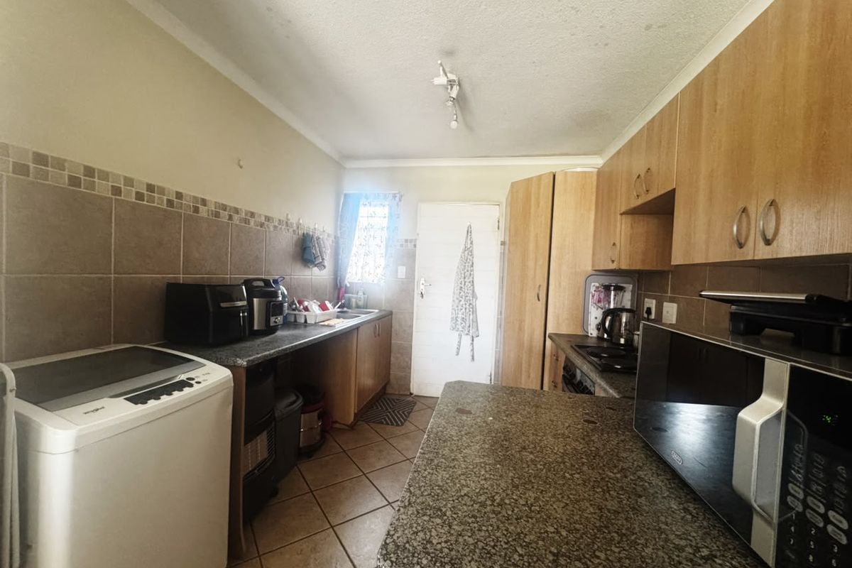 A functional kitchen featuring wood-finish cabinetry, granite countertops, tiled backsplash, and ceramic floor tiles, providing a practical workspace with integrated appliances.