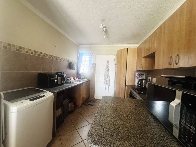 A functional kitchen featuring wood-finish cabinetry, granite countertops, tiled backsplash, and ceramic floor tiles, providing a practical workspace with integrated appliances.