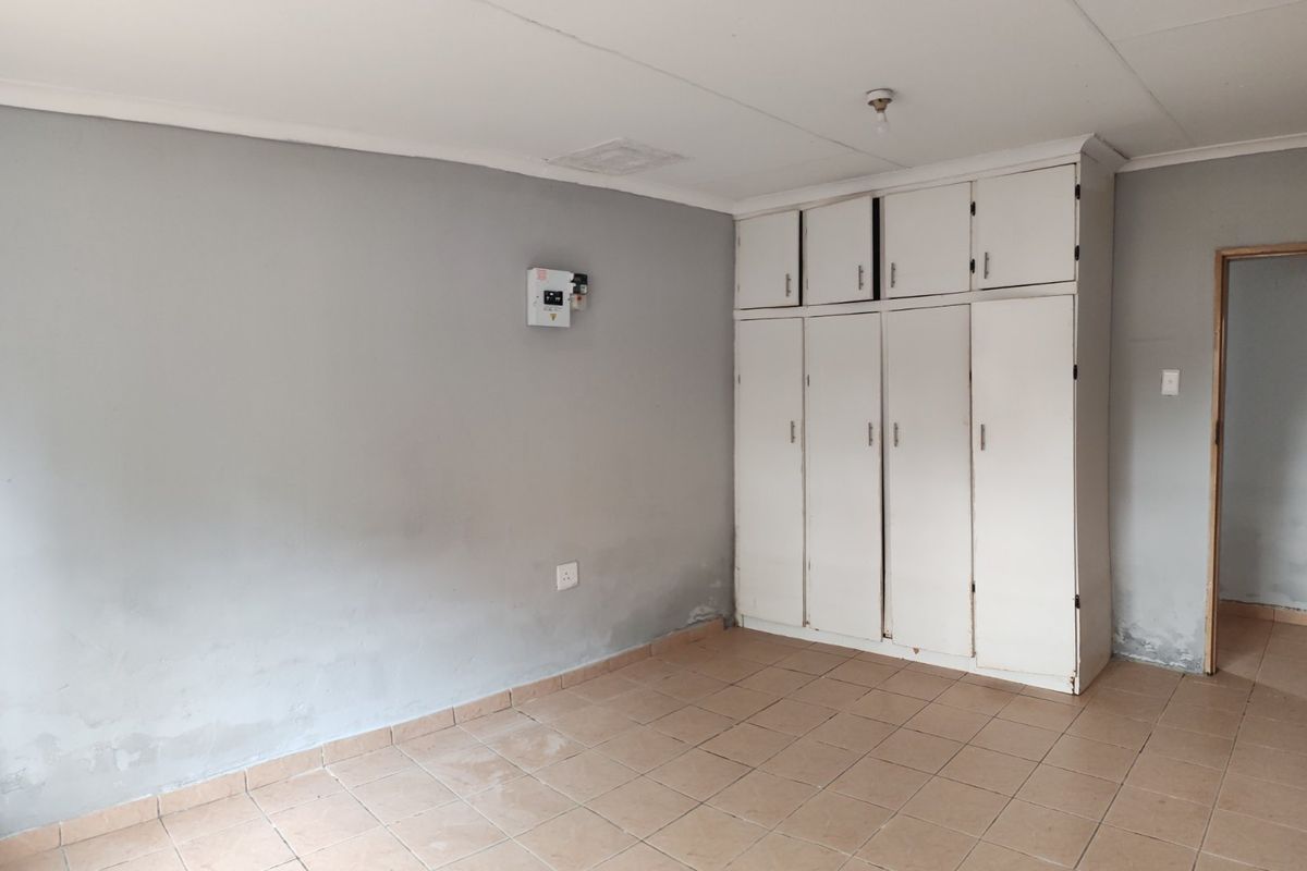An empty bedroom featuring built-in cupboards, tiled flooring, and an electrical distribution board. The room requires cosmetic updates to address wall and floor wear.