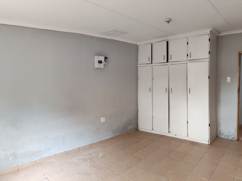 An empty bedroom featuring built-in cupboards, tiled flooring, and an electrical distribution board. The room requires cosmetic updates to address wall and floor wear.
