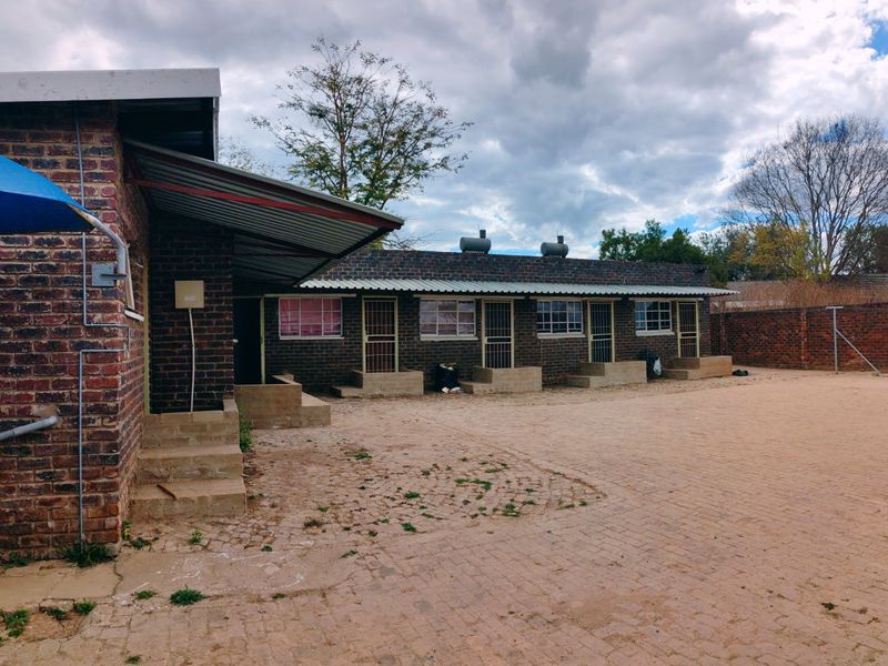 Rear exterior view of a face brick building featuring a large paved courtyard and multiple individual access points with security gates.