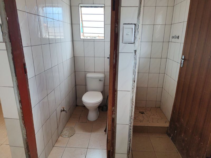 A functional bathroom featuring a toilet and a separate shower area with tiled finishes, requiring cosmetic updates to the door frames and wall edges.