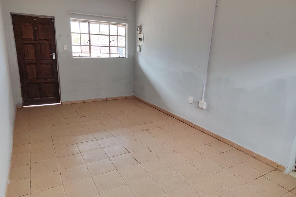 An empty, neutrally painted living area featuring tiled flooring, a timber door, and a window with security bars.