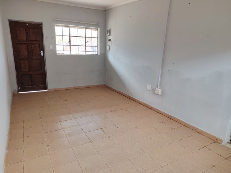 An empty, neutrally painted living area featuring tiled flooring, a timber door, and a window with security bars.