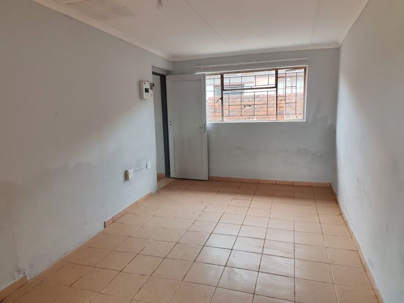 An empty bedroom featuring tiled flooring, security bars on the window, and an exposed electrical distribution board, requiring cosmetic updates to the wall finishes.