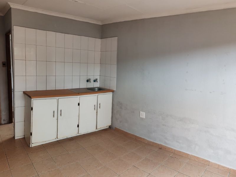 A compact, empty kitchen area featuring basic base cabinetry, a sink, tiled splashback, and tiled flooring, requiring cosmetic updates.