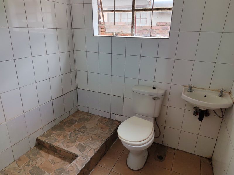 A dated bathroom featuring a toilet, wall-mounted basin, and a raised shower area with tiled finishes throughout.