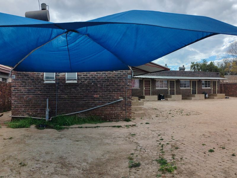Rear exterior view of the property featuring a brick facade, paved courtyard area, and a large blue shade sail structure.