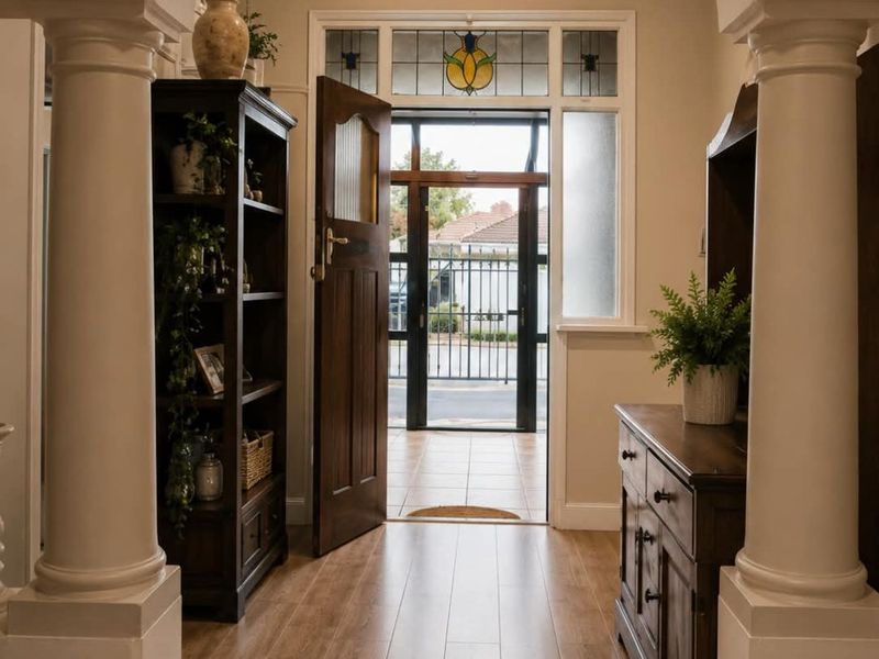 Welcoming entrance hall featuring an elegant arched walkway with decorative columns, timber flooring, and a classic front door with stained glass detailing.
