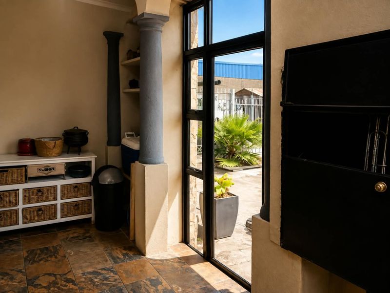 A covered patio area featuring stone tile flooring, decorative columns, and a built-in braai, with direct access to the outdoor garden space.