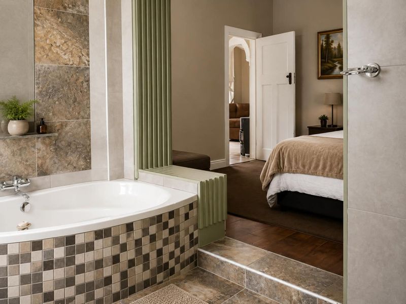 A well-maintained bathroom featuring a built-in bathtub with decorative mosaic tiling and stone-look wall accents, seamlessly transitioning into an adjacent bedroom.