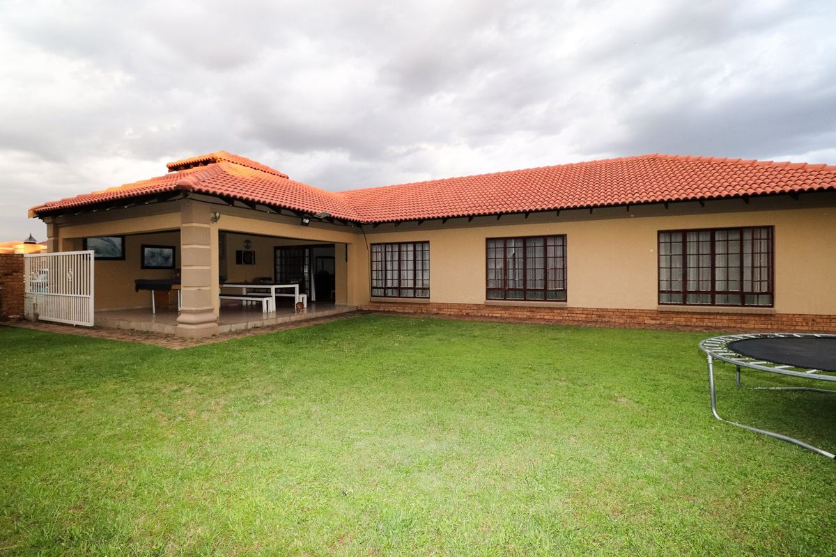 Rear view of the house featuring a covered patio area, terracotta tiled roof, and a well-maintained lawn.