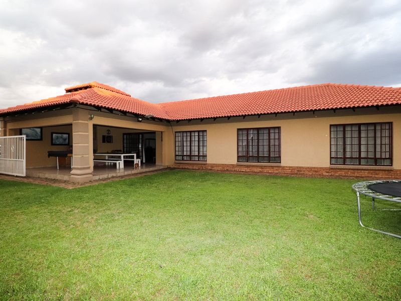 Rear view of the house featuring a covered patio area, terracotta tiled roof, and a well-maintained lawn.
