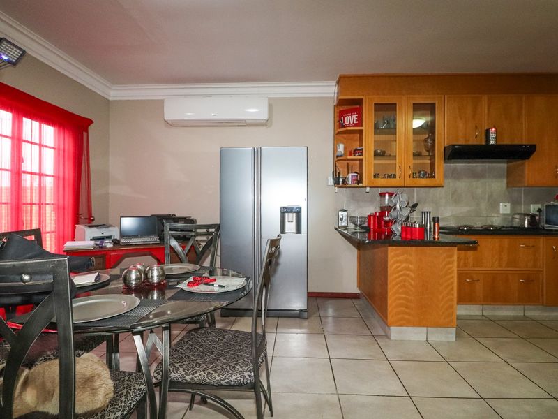 Open-plan kitchen and dining area featuring wooden cabinetry, granite countertops, tiled flooring, and a wall-mounted air conditioning unit.