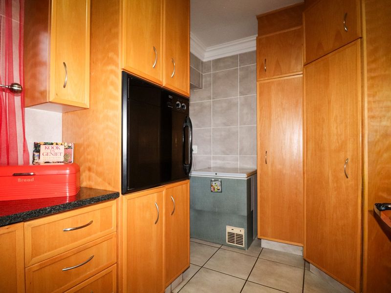A functional scullery area featuring extensive built-in wooden cabinetry, a built-in oven, and tiled finishes, providing ample storage and preparation space.