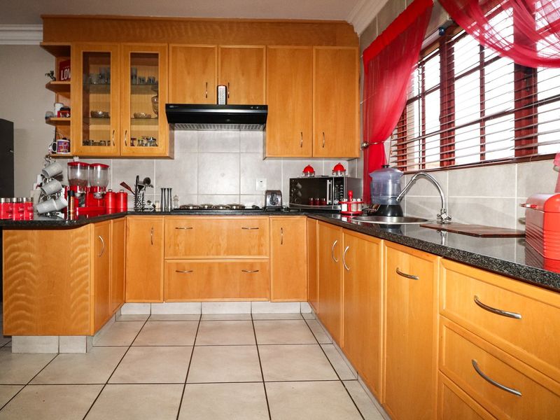 A functional kitchen featuring wooden cabinetry, granite countertops, a built-in hob with extractor fan, and tiled flooring.