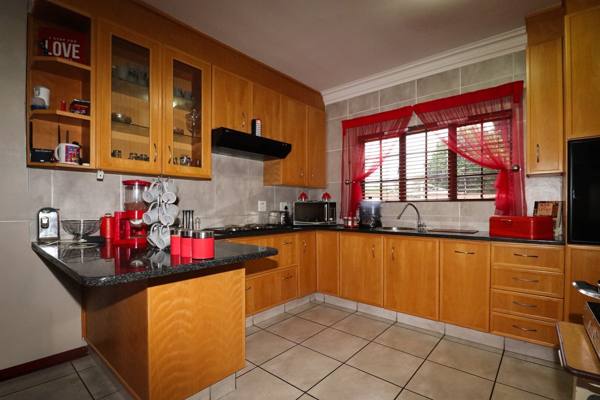 A functional kitchen featuring wooden cabinetry, granite countertops, a built-in hob with extractor fan, and tiled finishes throughout.