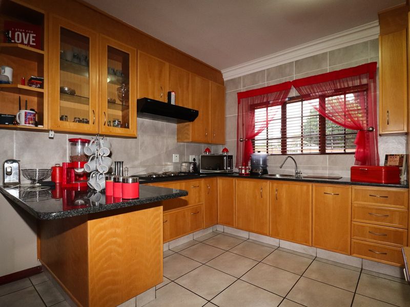 A functional kitchen featuring wooden cabinetry, granite countertops, a built-in hob with extractor fan, and tiled finishes throughout.