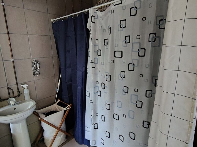 A functional bathroom featuring a pedestal basin, tiled walls and flooring, and a shower area enclosed by curtains.
