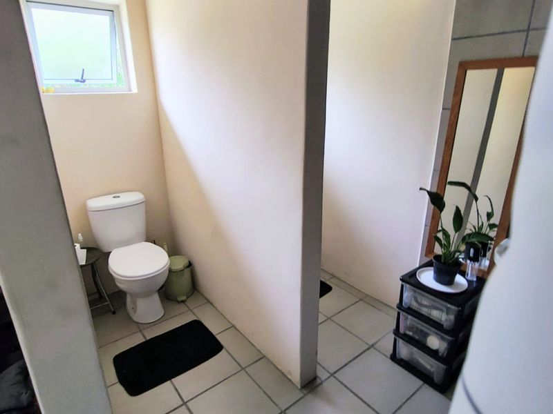 A functional bathroom featuring tiled flooring, a standard toilet, and a small casement window, offering a clean and practical layout.
