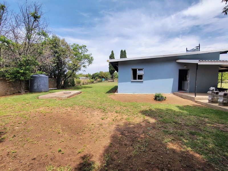 Rear view of the property featuring a spacious garden, water tank, concrete slab, and a covered patio area with a solar water heater installed.