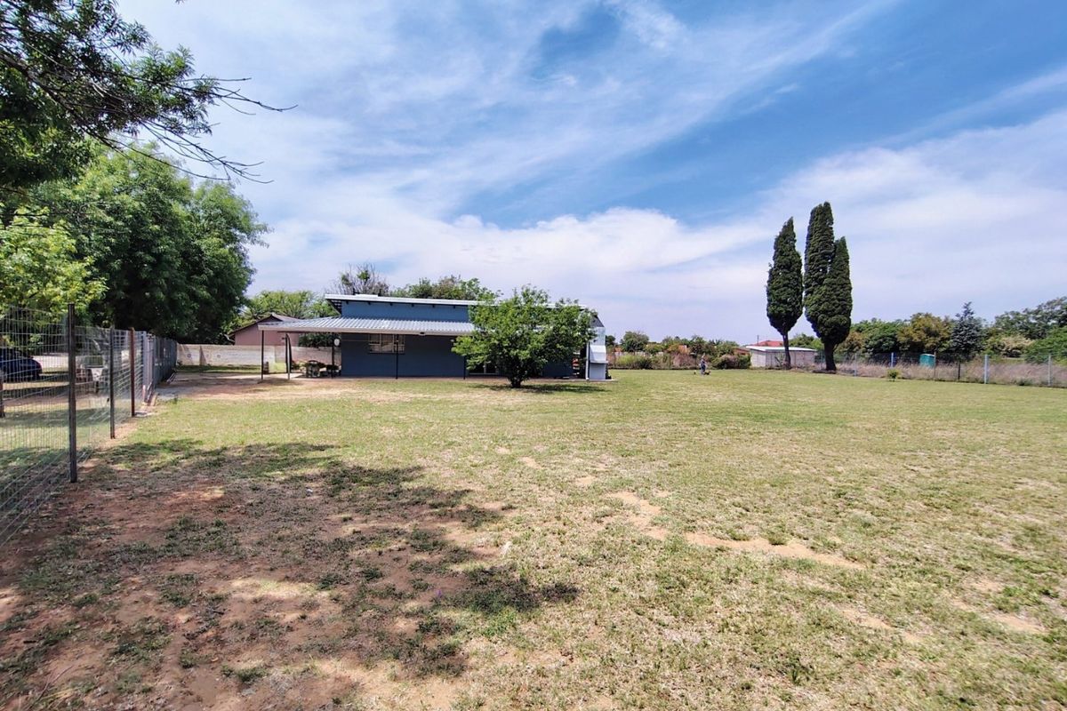 A spacious rear garden featuring a large lawn, wire mesh fencing, and a covered patio area attached to the main house structure.