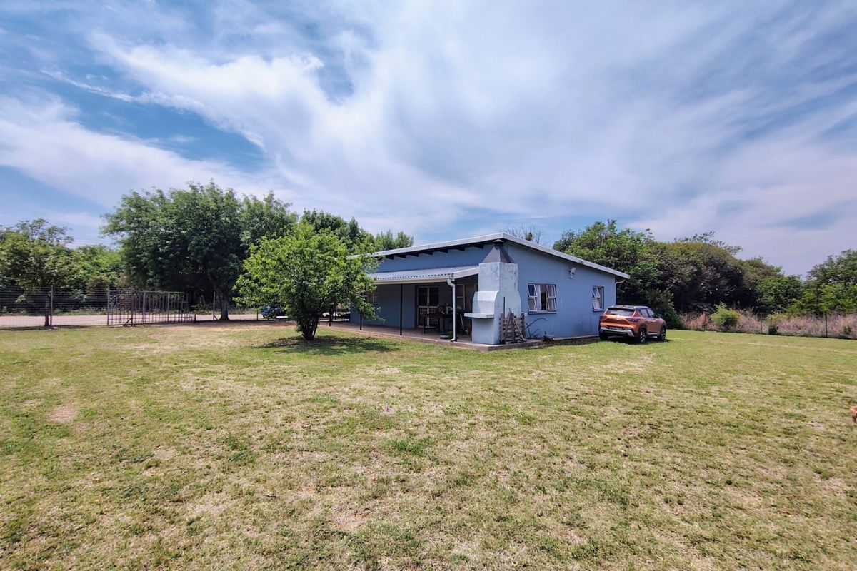 Rear view of the house featuring a covered patio area with a built-in braai, set within a spacious garden with perimeter fencing.