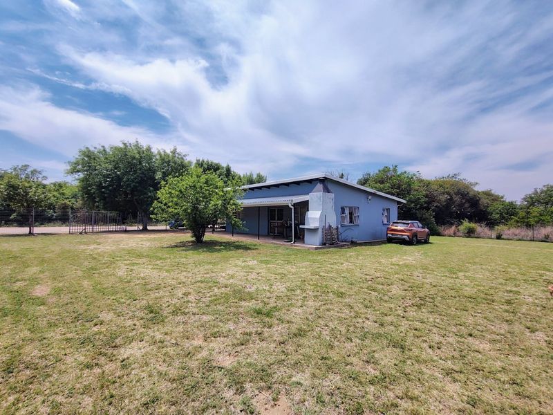 Rear view of the house featuring a covered patio area with a built-in braai, set within a spacious garden with perimeter fencing.