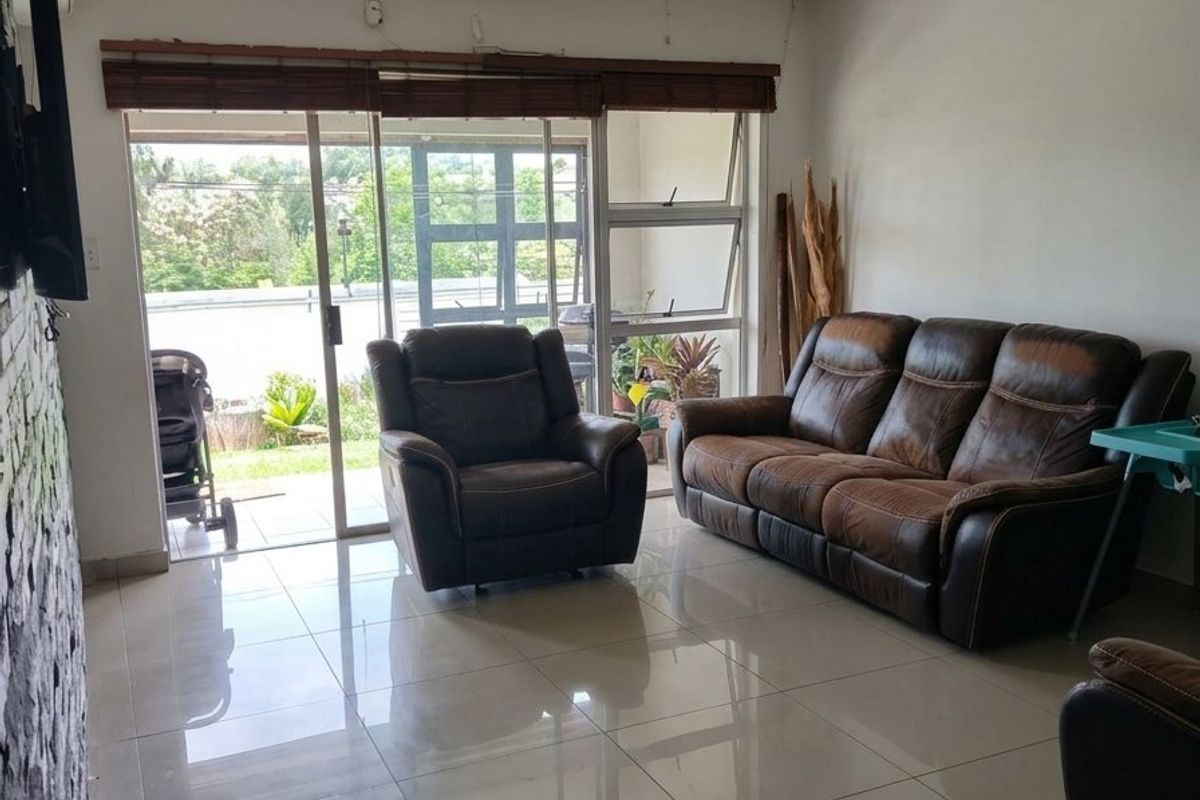 A living room featuring large format floor tiles, a stone accent wall, and sliding glass doors leading to an outdoor area.