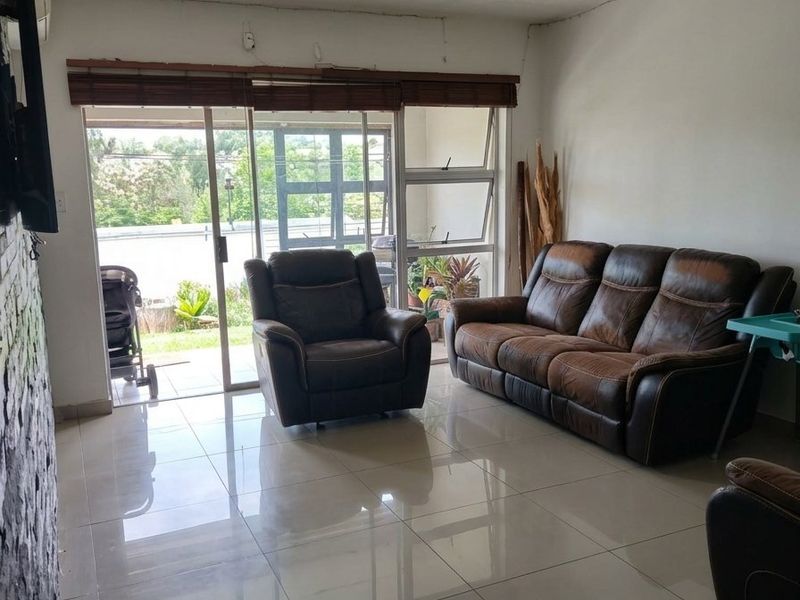 A living room featuring large format floor tiles, a stone accent wall, and sliding glass doors leading to an outdoor area.