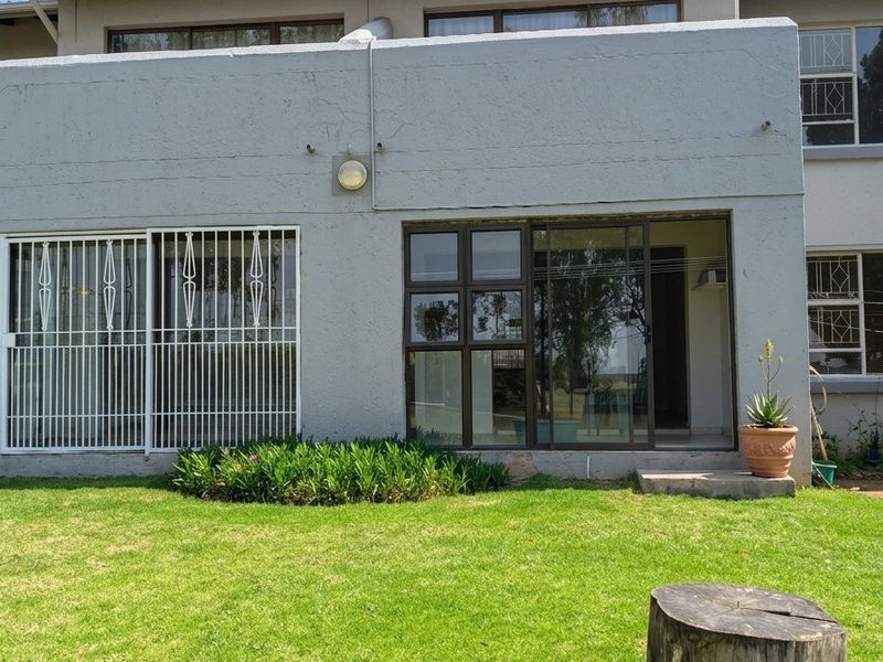 Rear view of the apartment featuring a private lawn, sliding glass doors with security gates, and aluminium window frames.
