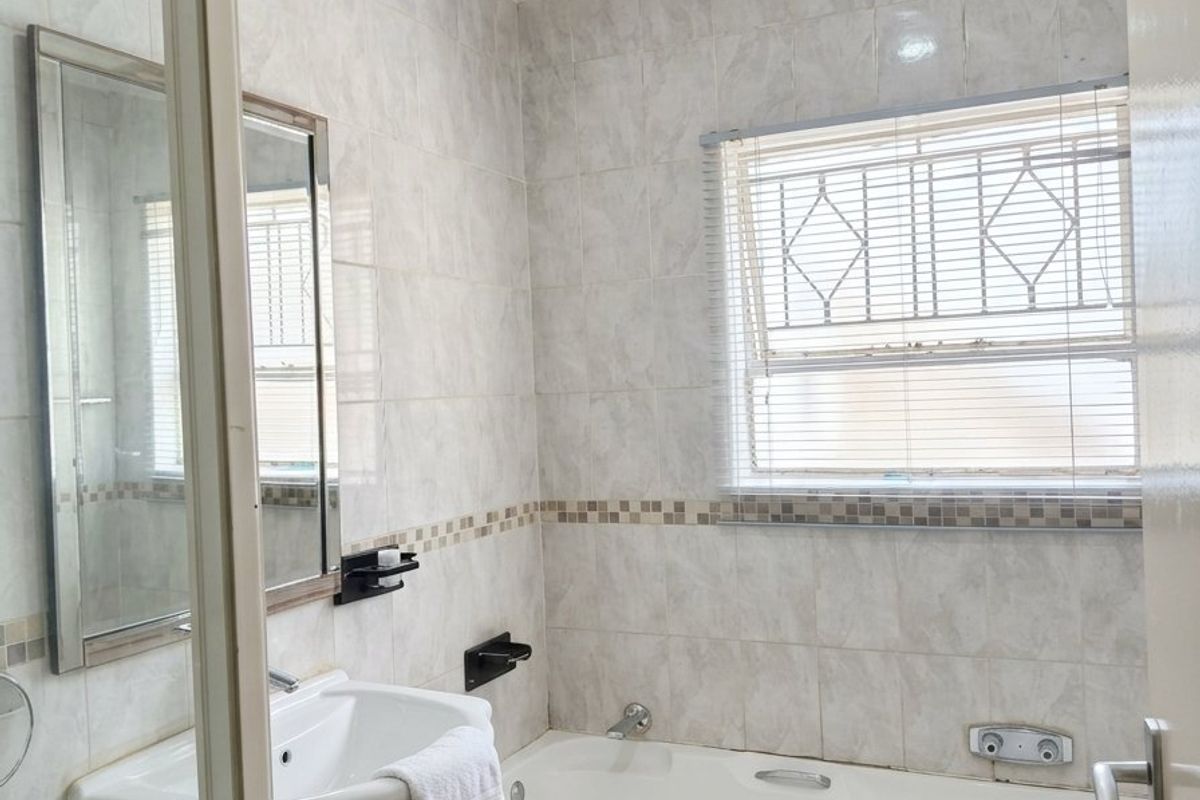 A functional bathroom featuring a built-in vanity, bathtub, shower enclosure, and tiled finishes, offering a practical layout with potential for modern updates.