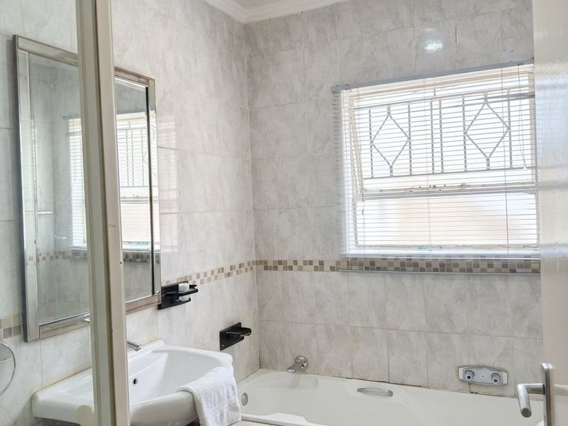 A functional bathroom featuring a built-in vanity, bathtub, shower enclosure, and tiled finishes, offering a practical layout with potential for modern updates.