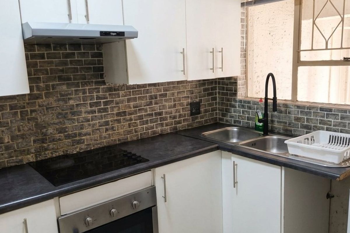 Modern kitchen featuring white cabinetry, dark laminate countertops, a built-in oven with electric hob, and a stylish brick-patterned tiled backsplash.