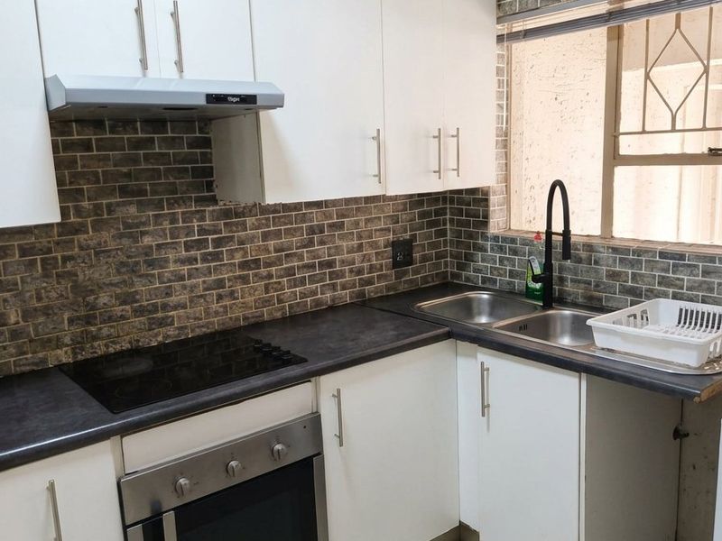 Modern kitchen featuring white cabinetry, dark laminate countertops, a built-in oven with electric hob, and a stylish brick-patterned tiled backsplash.