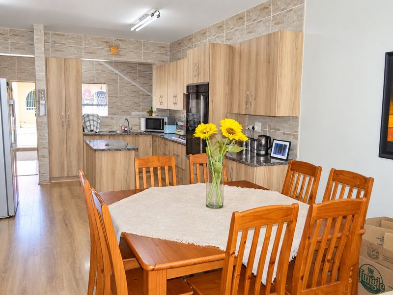 Open-plan kitchen and dining area featuring light wood cabinetry, granite countertops, and modern tiled backsplash, creating a functional and cohesive living space.