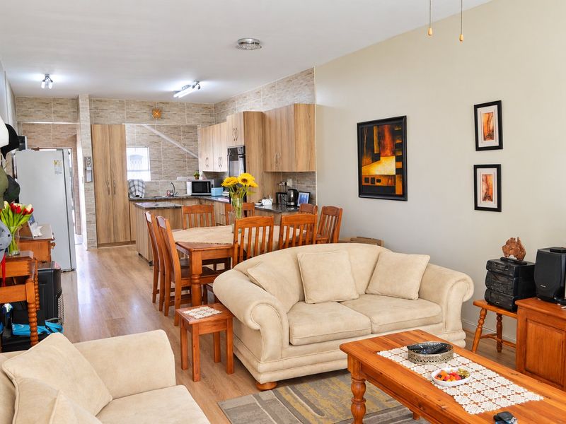 An open-plan living and dining area featuring laminate flooring, neutral walls, and a functional kitchen with built-in cabinetry and stone-look tile accents.