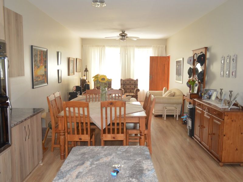 Open-plan living and dining area featuring laminate flooring, a ceiling fan, and a functional kitchen with built-in oven and granite countertops.