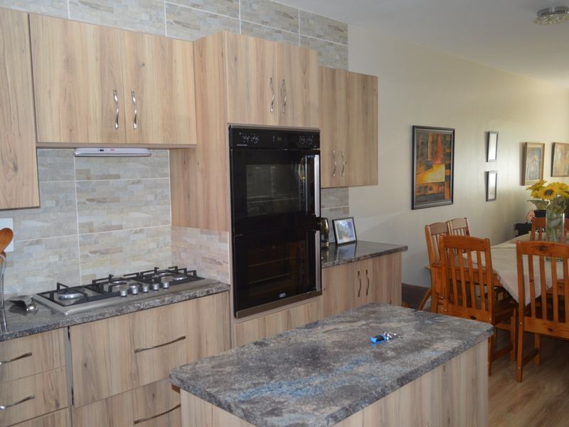 Open-plan kitchen featuring modern wood-look cabinetry, stone-look countertops, a gas hob, built-in double oven, and a functional kitchen island.