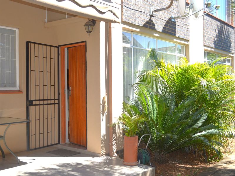 A covered patio area featuring a security gate, retractable awning, and direct access to the apartment interior through a wooden door.
