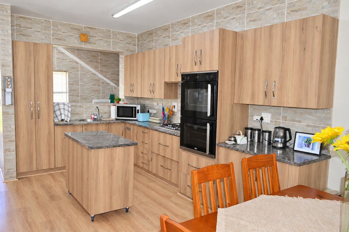 A functional kitchen featuring wood-look cabinetry, stone-effect countertops, a double wall oven, and a convenient mobile kitchen island with matching finishes.