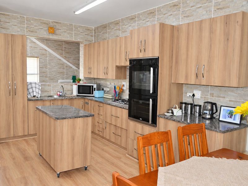 A functional kitchen featuring wood-look cabinetry, stone-effect countertops, a double wall oven, and a convenient mobile kitchen island with matching finishes.