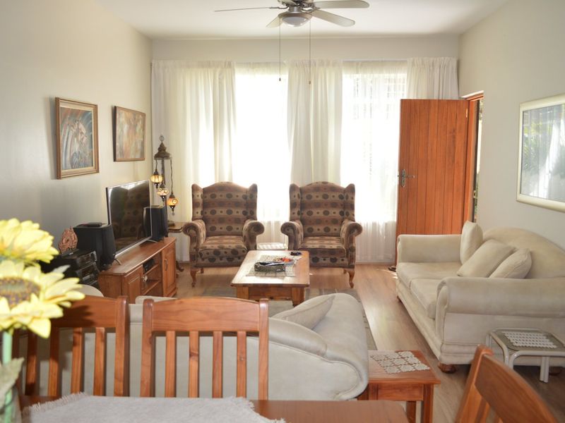 A comfortable living room featuring laminate flooring, a ceiling fan, and direct access to an outdoor area through a wooden door.