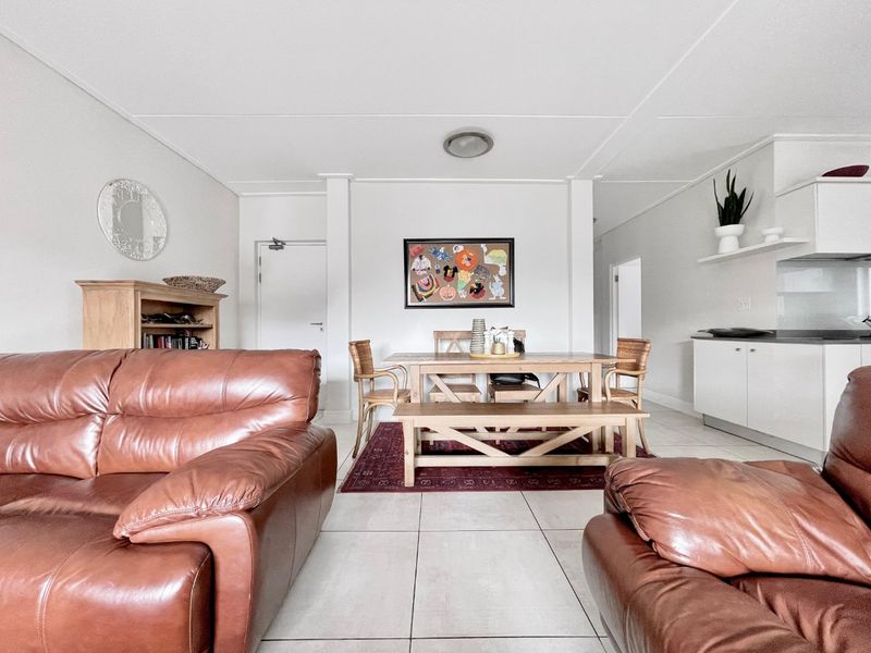 An open-plan living and dining area featuring neutral tiled flooring, clean white walls, and a functional kitchen space with built-in cabinetry.