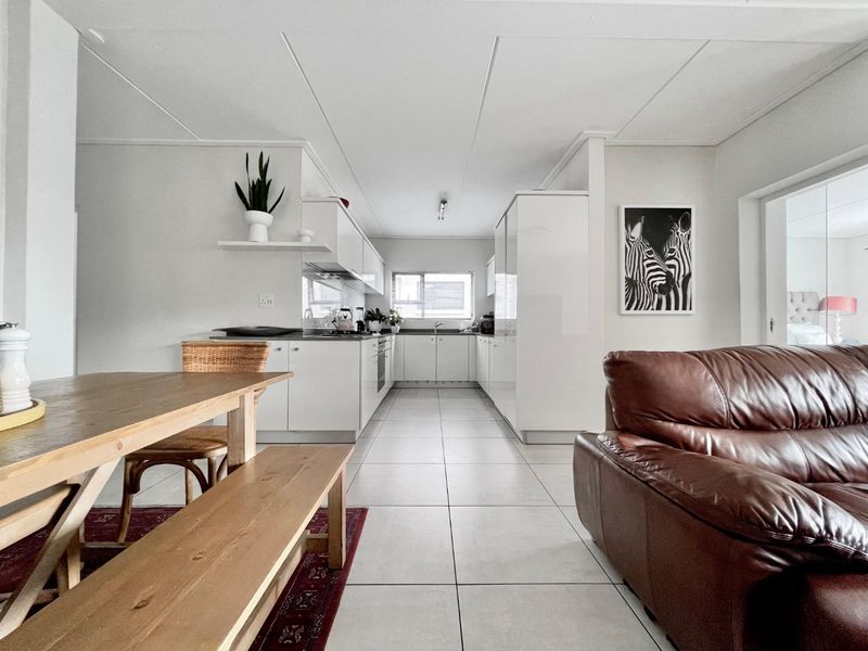 A bright open-plan living and kitchen area featuring modern white cabinetry, tiled flooring, and a functional layout suitable for contemporary apartment living.