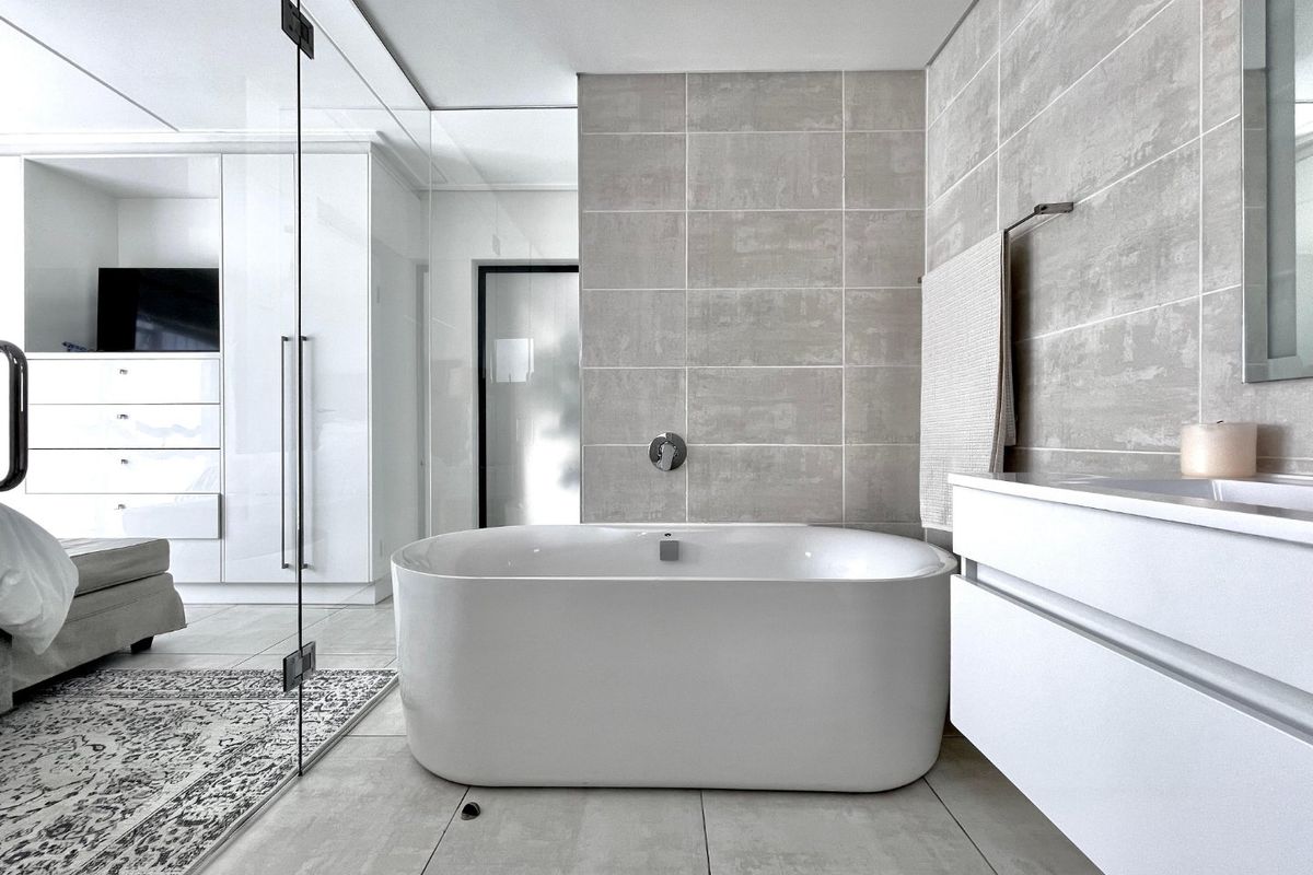 Modern bathroom featuring a sleek freestanding bathtub, wall-mounted faucet, floating vanity, and glass shower partition with contemporary neutral tiling.