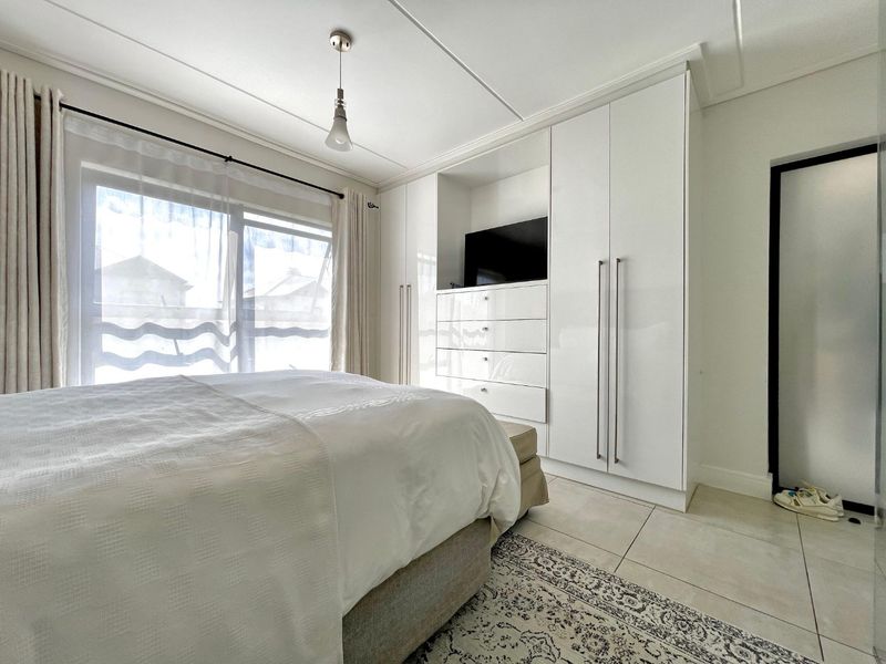 A bright and modern bedroom featuring sleek white built-in cupboards, tiled flooring, and a sliding glass door that allows for ample natural light.
